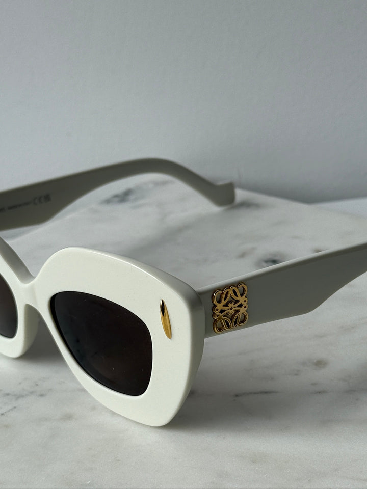 White cat-eye sunglasses with dark lenses and gold logo on temple