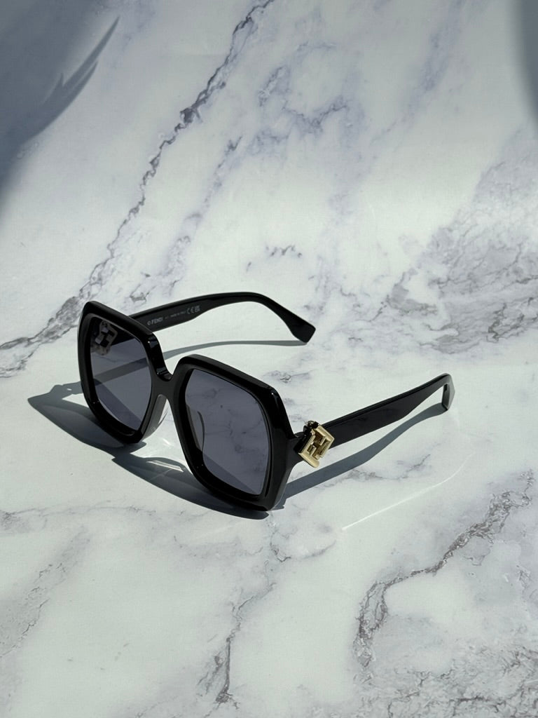 Black square sunglasses with dark lenses, gold logo bridge, angled side view