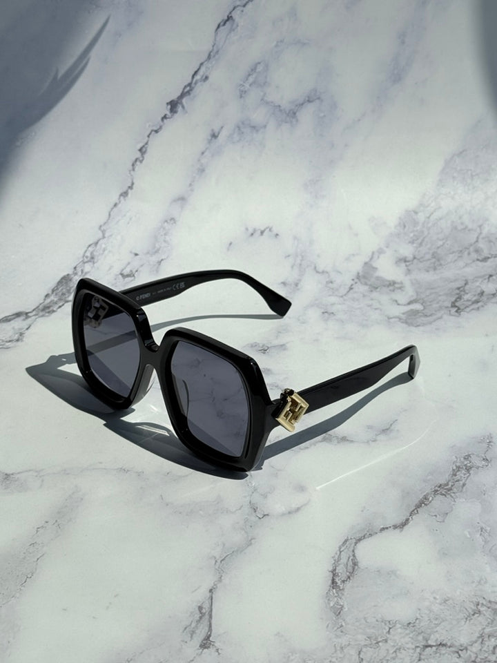 Black square sunglasses with dark lenses, gold logo bridge, angled side view