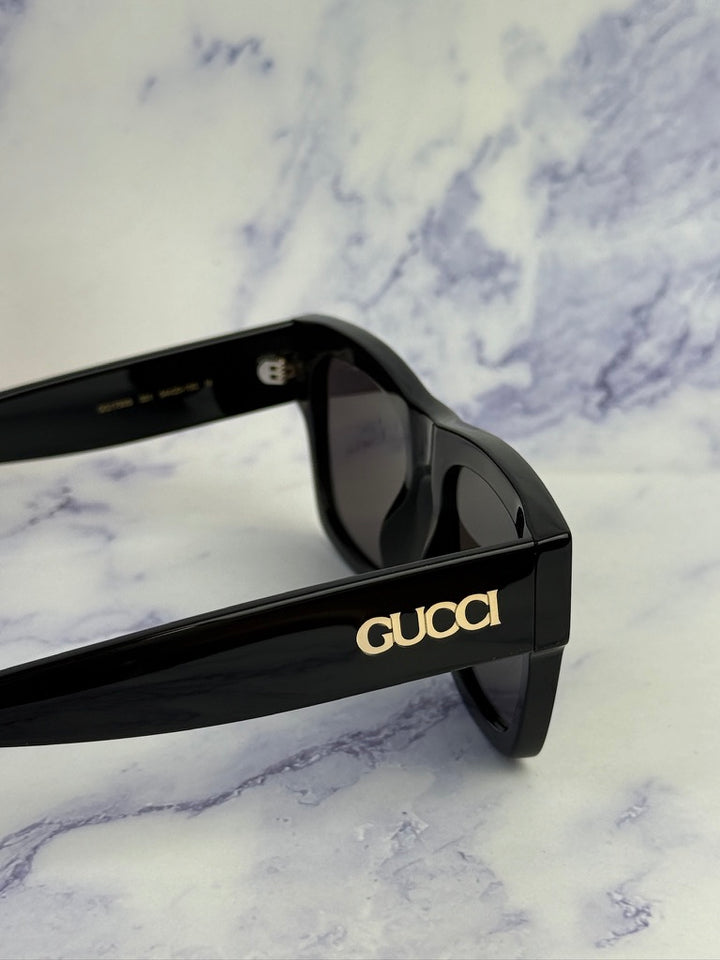 Black Gucci sunglasses with dark lenses and Gucci name on hinge arm