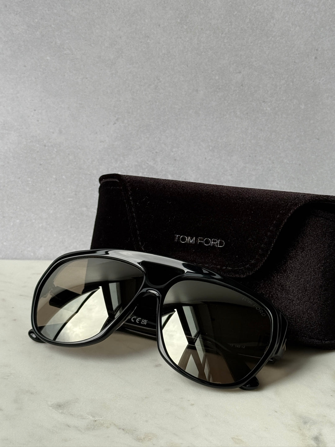 Black aviator sunglasses with mirrored lenses, TOM FORD logo case behind