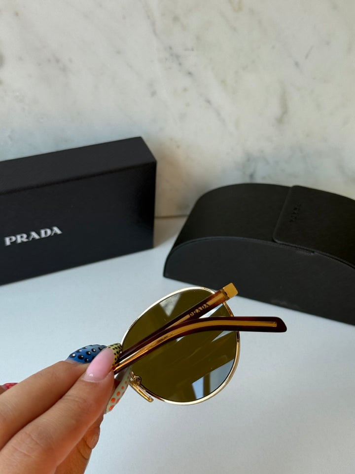 Prada round sunglasses laid out, gold frame with dark brown lenses and brown inner arms