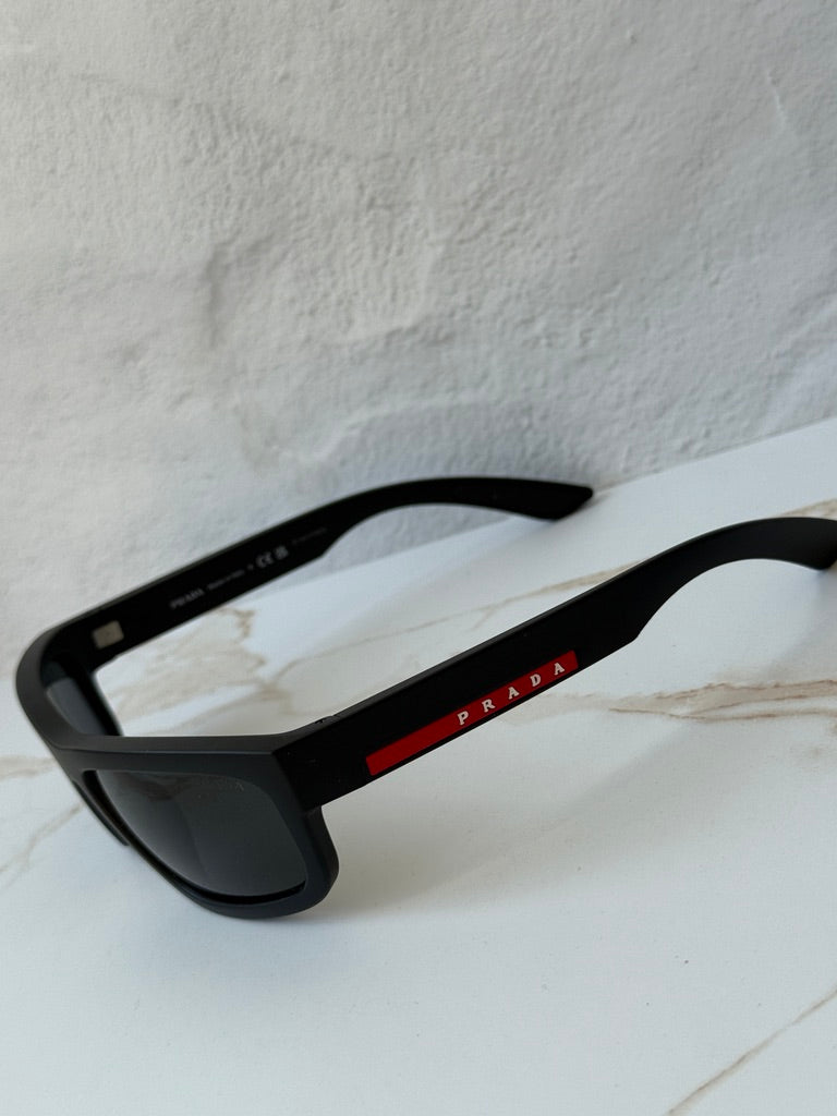 Black Prada Sport sunglasses with dark lenses and red Prada logo on temple