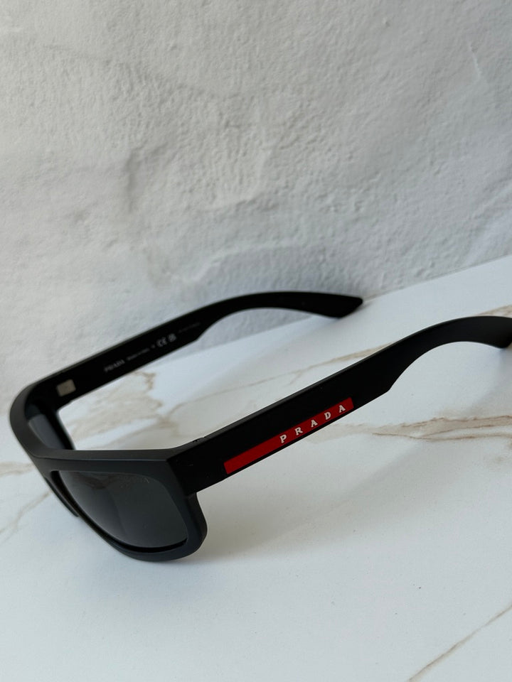 Black Prada Sport sunglasses with dark lenses and red Prada logo on temple