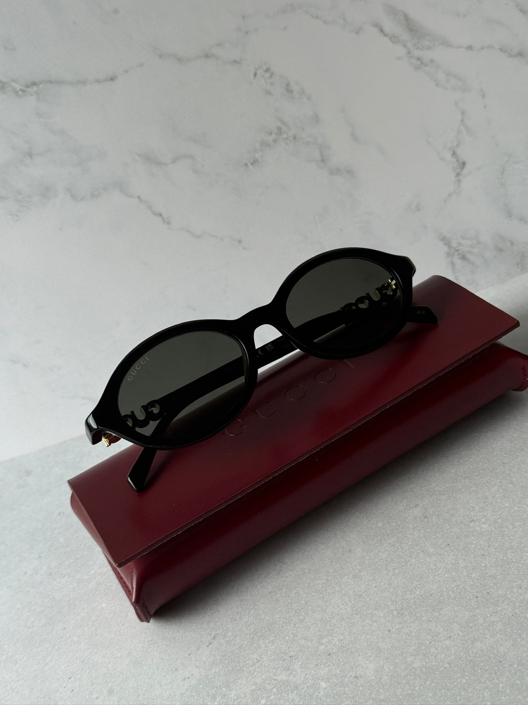 Black oval sunglasses with dark lenses resting on maroon case