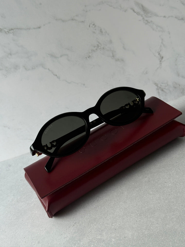 Black oval sunglasses with dark lenses resting on maroon case