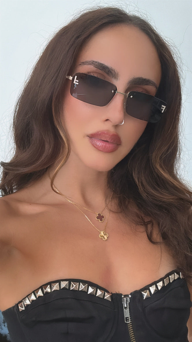 Black rimless sunglasses with gold metal frame and dark lenses on a model