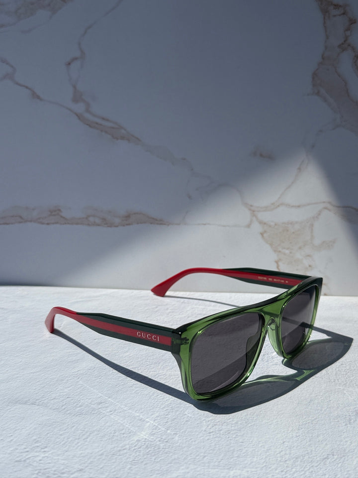 Gucci striped green sunglasses with dark lenses and red temples, angled view.