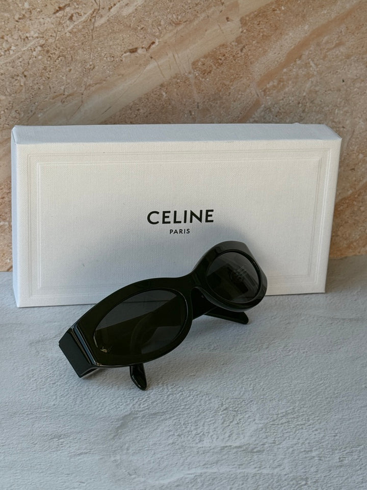 Black cat-eye sunglasses with dark lenses, resting on white display box