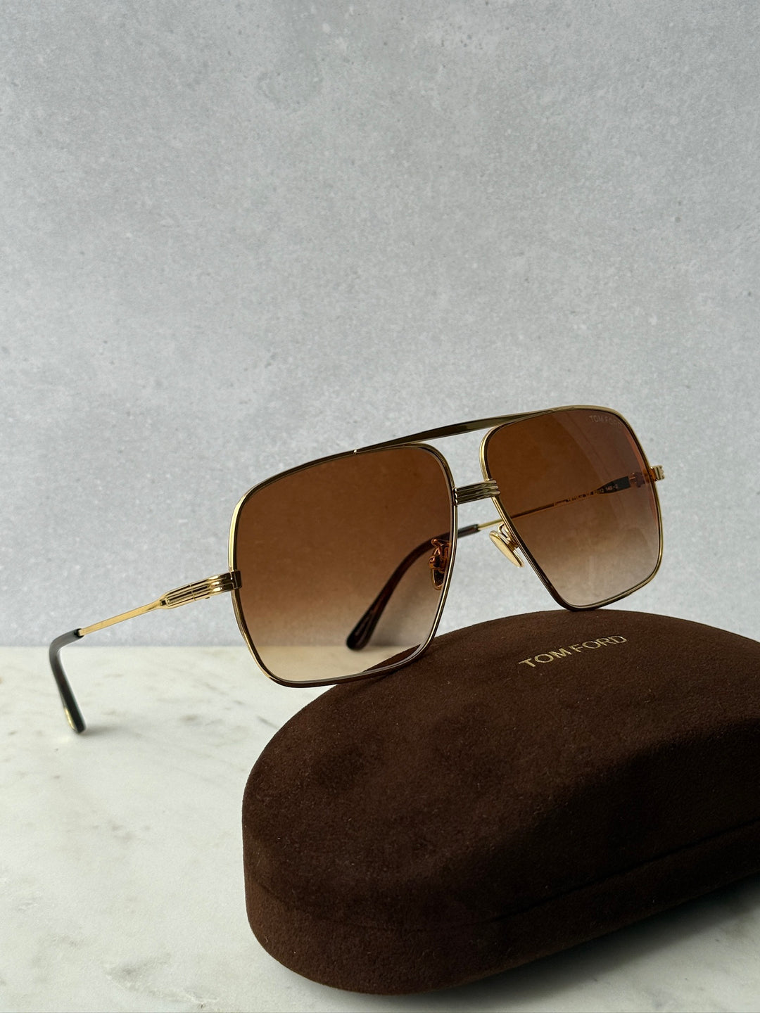Gold-tone aviator sunglasses with brown lenses on case, side angle
