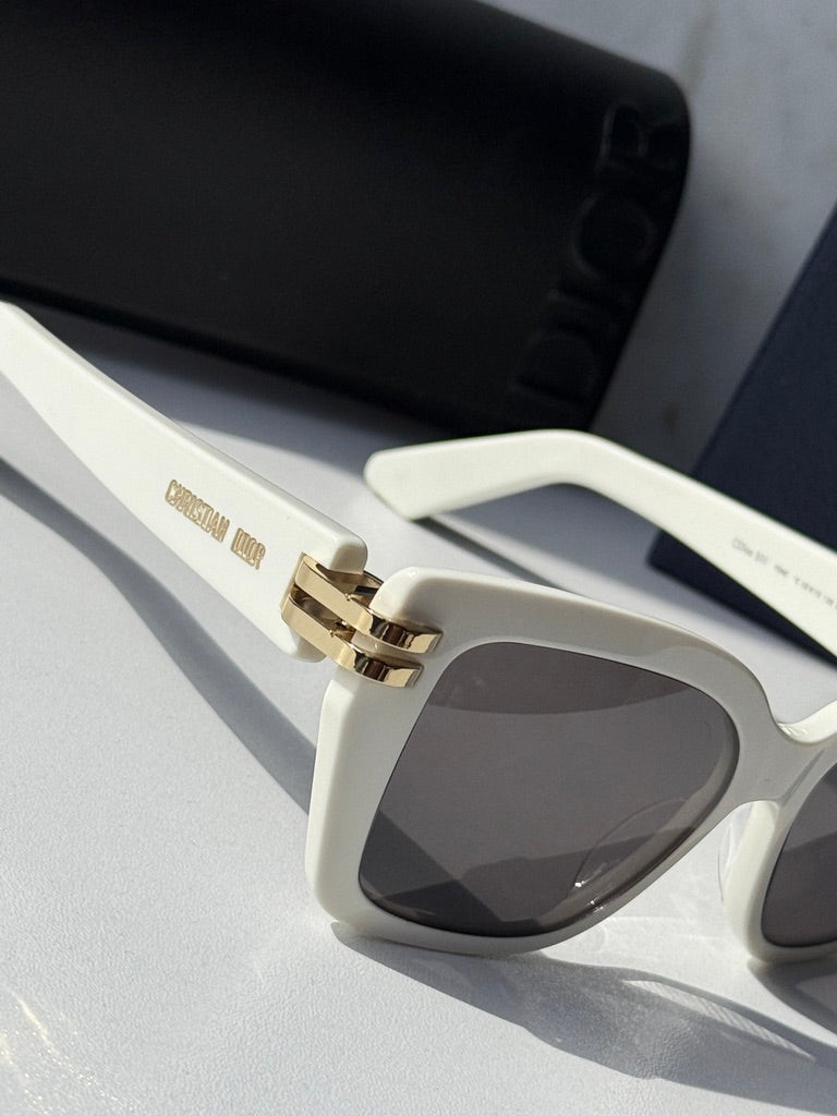 Oversized butterfly sunglasses close-up: white frame, gold hinge, dark lenses