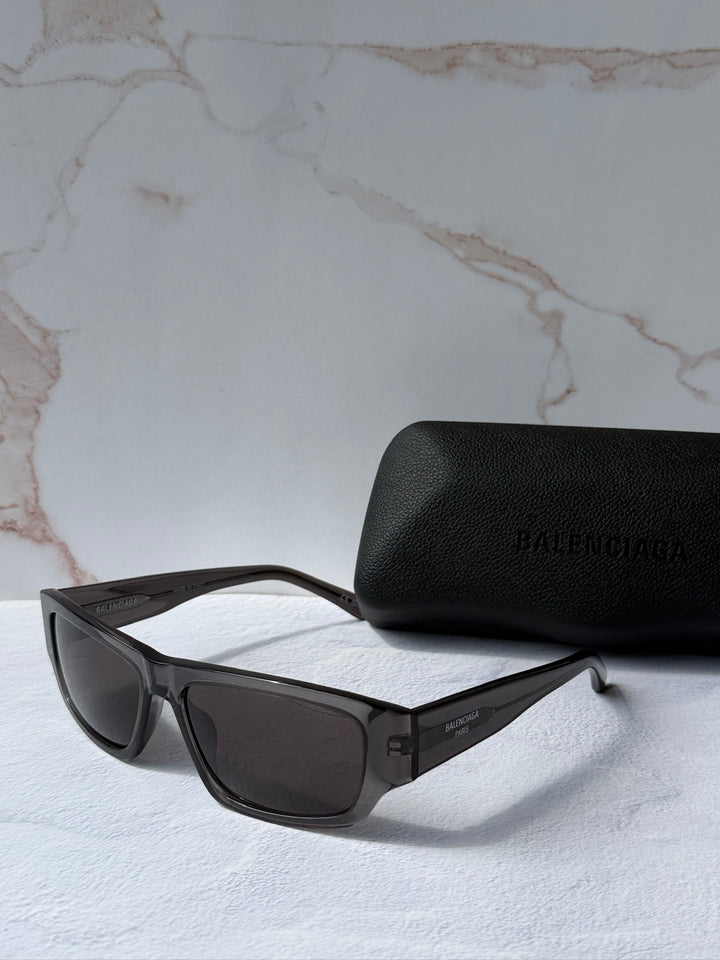 Balenciaga dark grey sunglasses with dark lenses next to black logo case