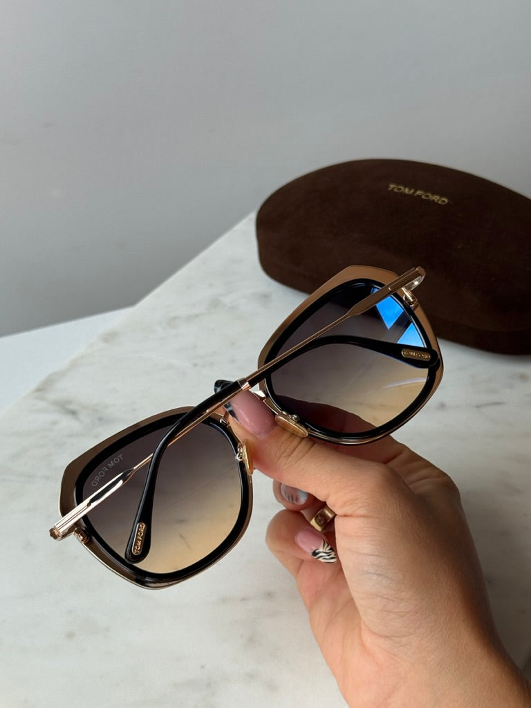 Tom Ford black and gold sunglasses held by hand, dark tinted lenses and metal bridge