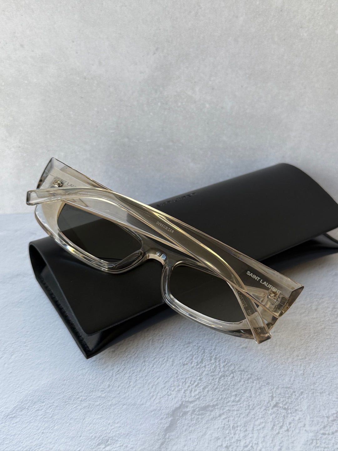 Saint Laurent SL553 slim sunglasses, transparent frame; angled view with black case