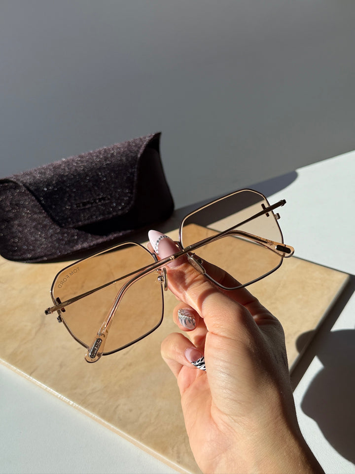 Square sunglasses with gold frame and amber lenses, held by hand
