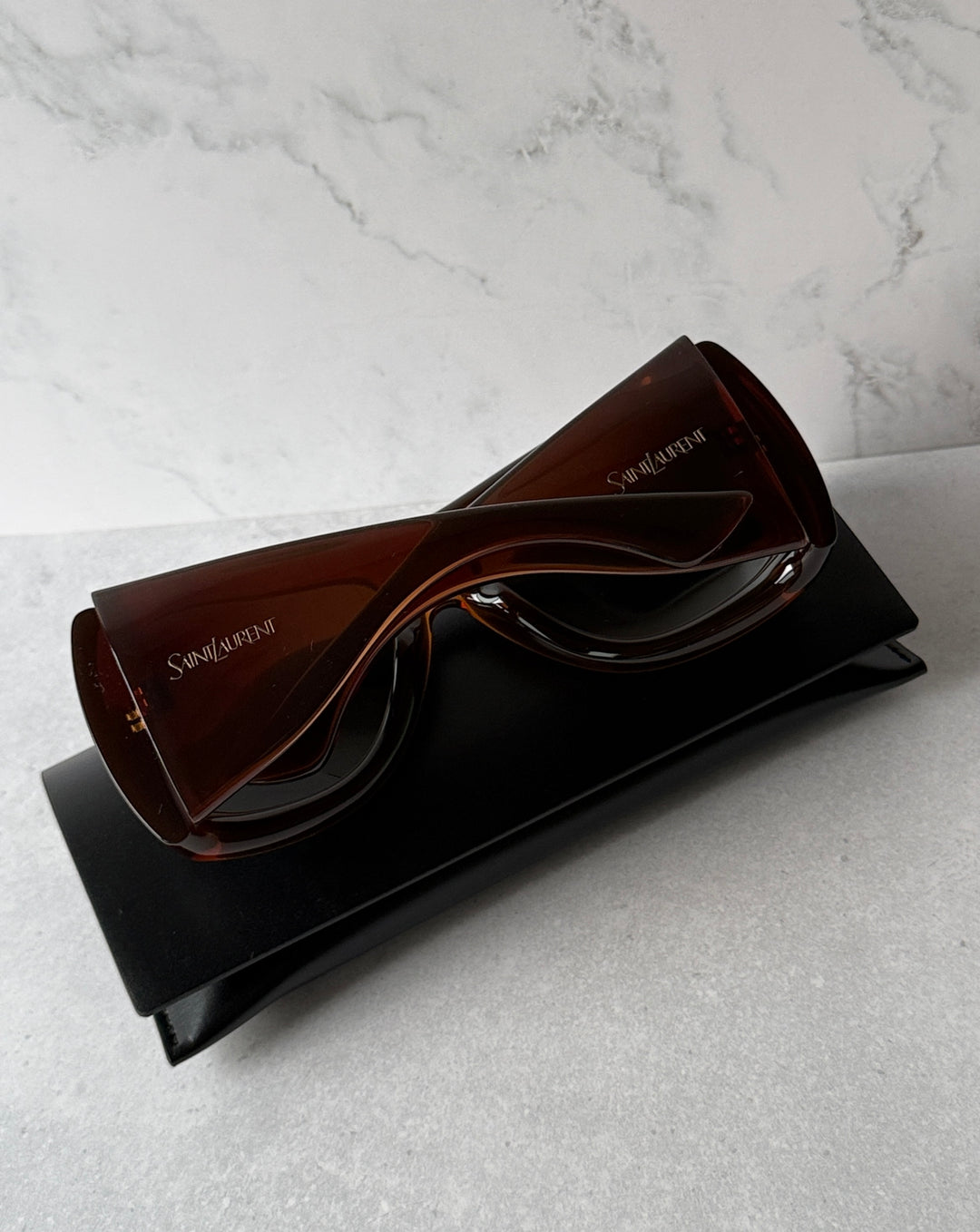 Brown Howl sunglasses with dark lenses, shown with temple logo on black case.