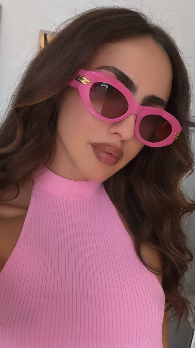 Pink sunglasses with dark lenses, gold hinge detail, worn by a person
