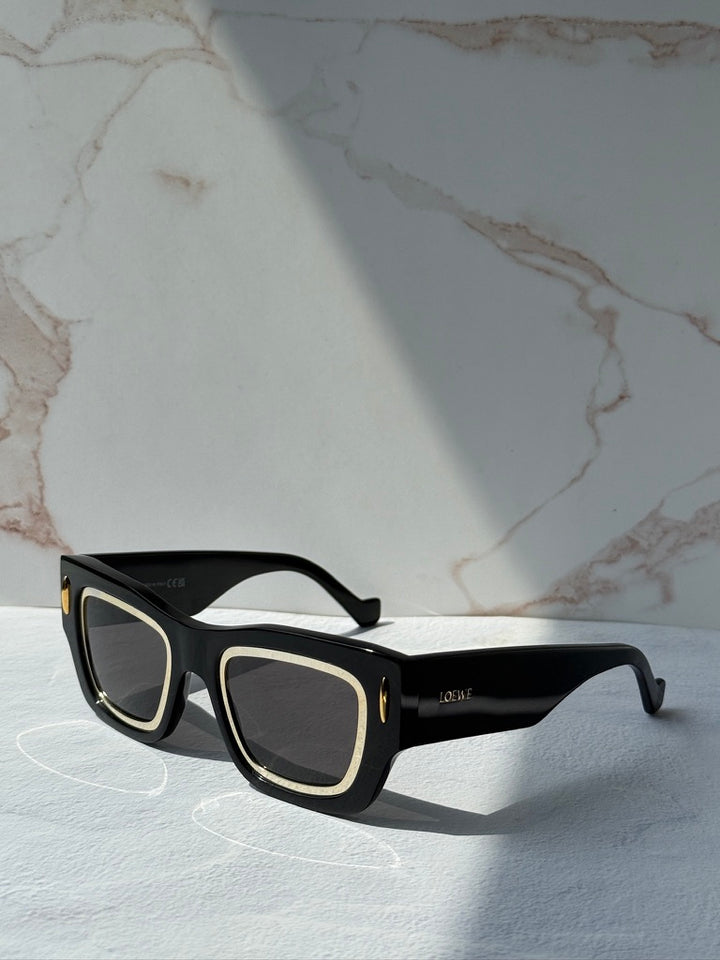 Black square sunglasses with dark lenses and gold-tone trim, shown at an angle.