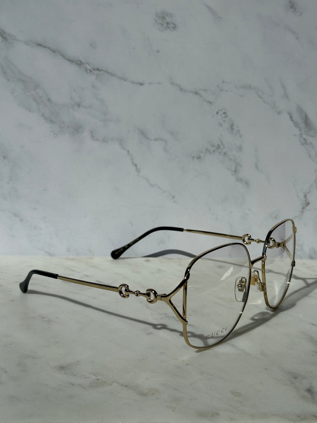 Gold metal eyeglass frames with horsebit detail, black arms, and clear lenses