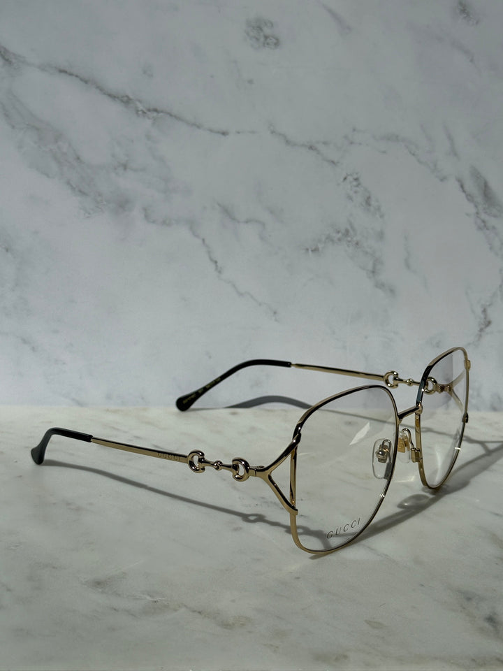 Gold metal eyeglass frames with horsebit detail, black arms, and clear lenses