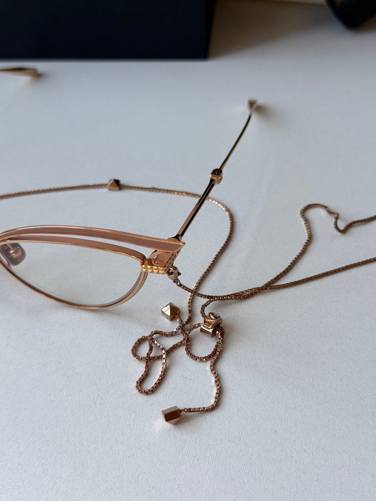 Close-up of gold-tone cat-eye eyeglass frames with beige lenses and chain details