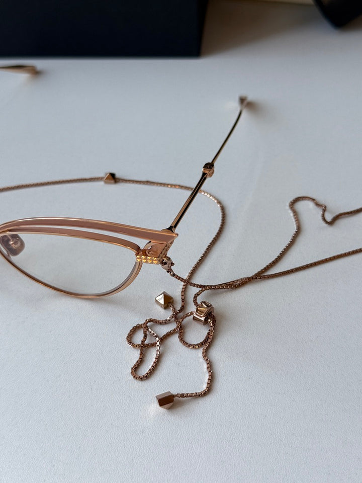 Close-up of gold-tone cat-eye eyeglass frames with beige lenses and chain details