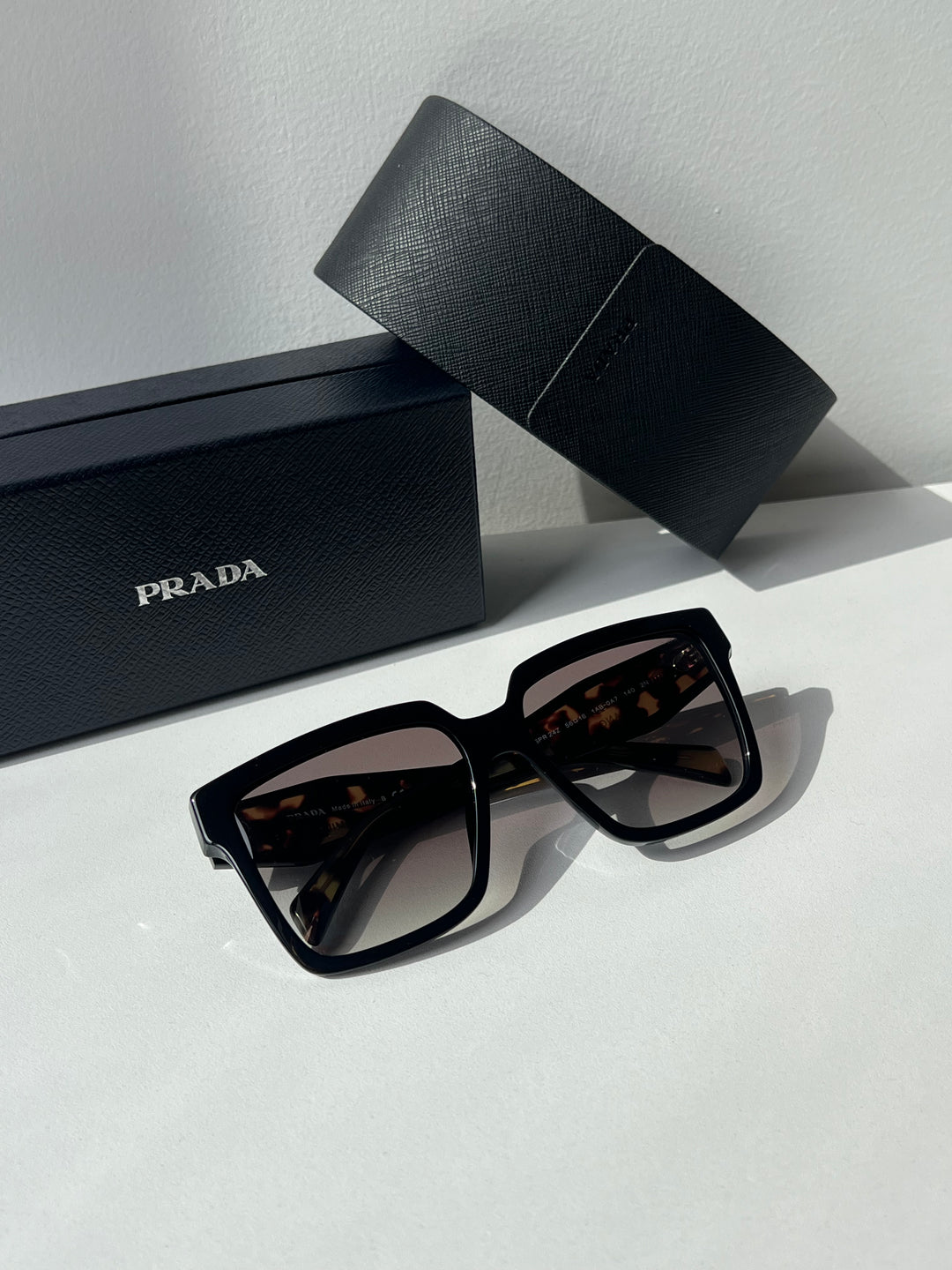 Prada oversized sunglasses with dark lenses beside black Prada gift case