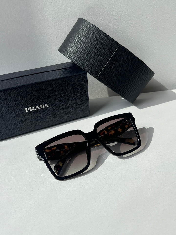 Prada oversized sunglasses with dark lenses beside black Prada gift case