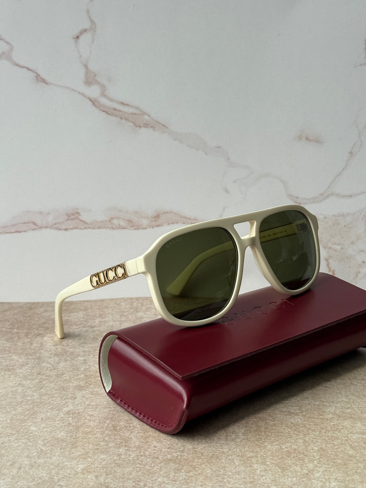 GUCCI aviator sunglasses with ivory frames and dark lenses, on burgundy case