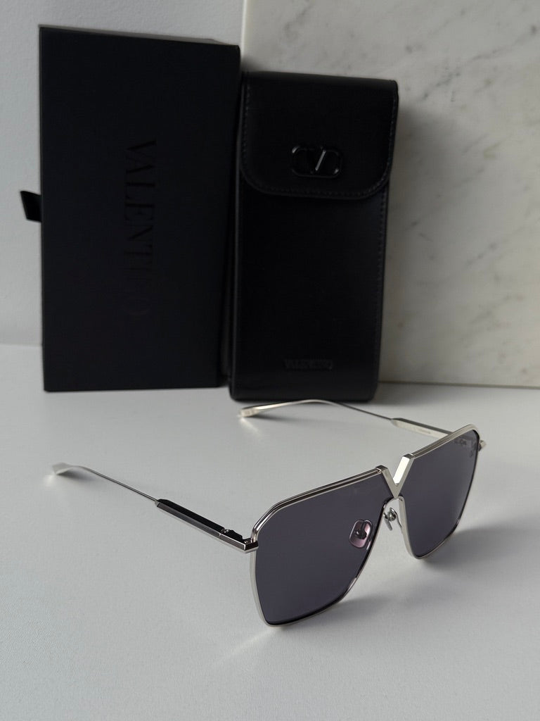 Silver aviator sunglasses with dark lenses and slim arms, beside black case