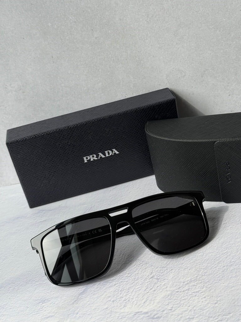 Black aviator sunglasses with dark lenses, PRADA logo on temple, in black case