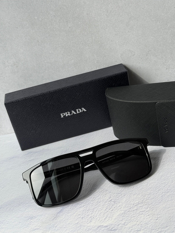 Black aviator sunglasses with dark lenses, PRADA logo on temple, in black case