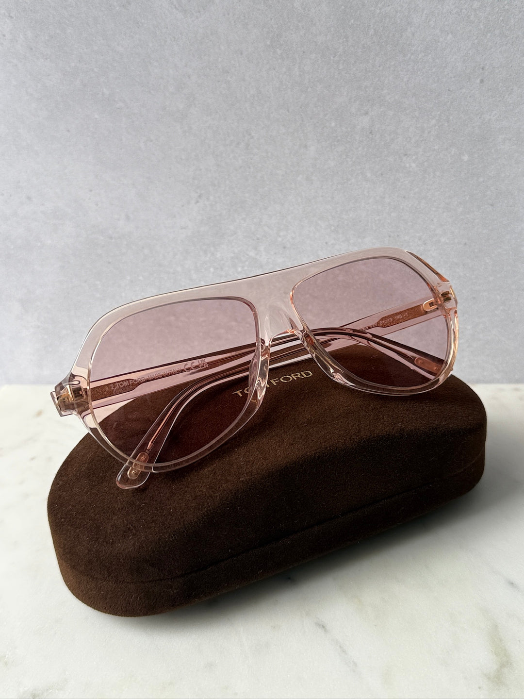 Pink aviator sunglasses with rose-tinted lenses on a soft case, angled view