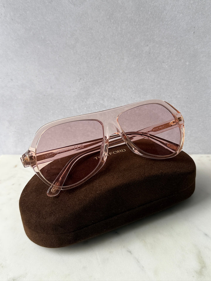 Pink aviator sunglasses with rose-tinted lenses on a soft case, angled view