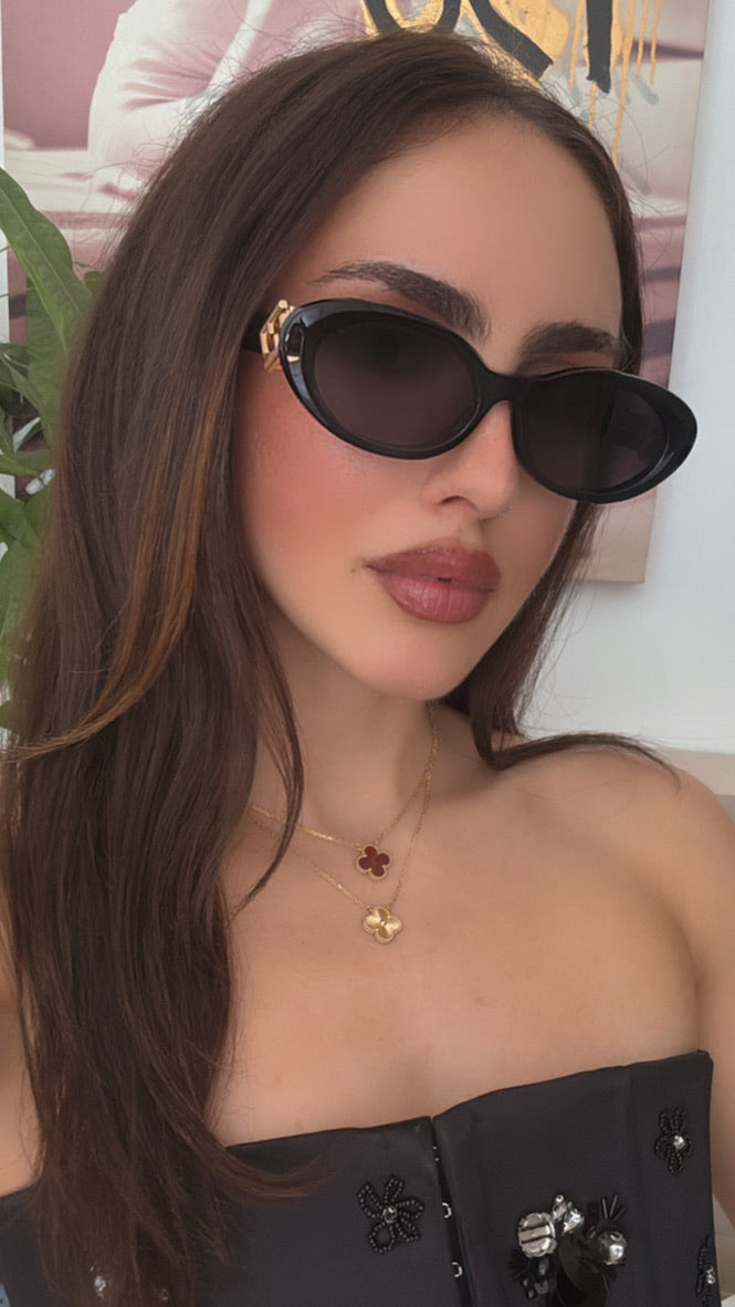 Black oval sunglasses with dark lenses and gold logo hinge, worn on model