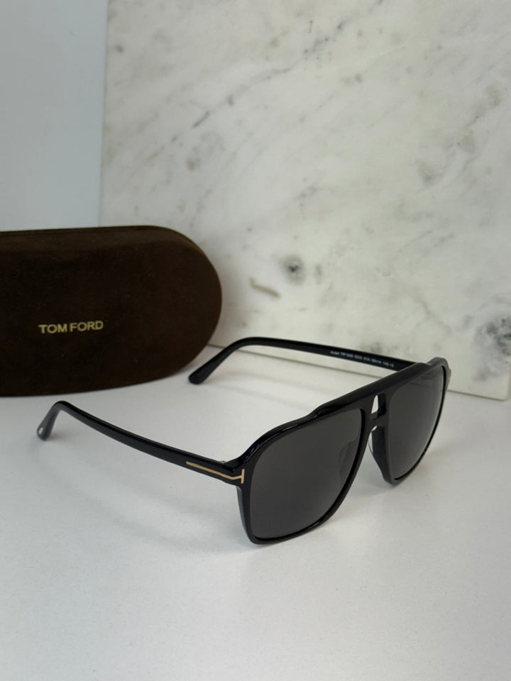 Black Tom Ford sunglasses with dark lenses, metal bar at hinge, case nearby.