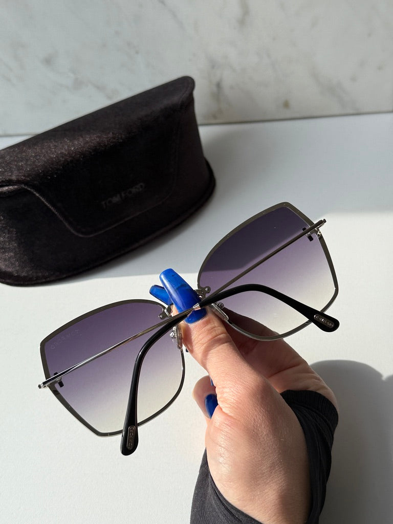 Silver grey sunglasses with dark gradient lenses held in a hand