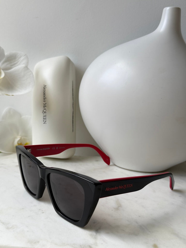 Black cat-eye sunglasses with dark lenses, red trim on temple arms