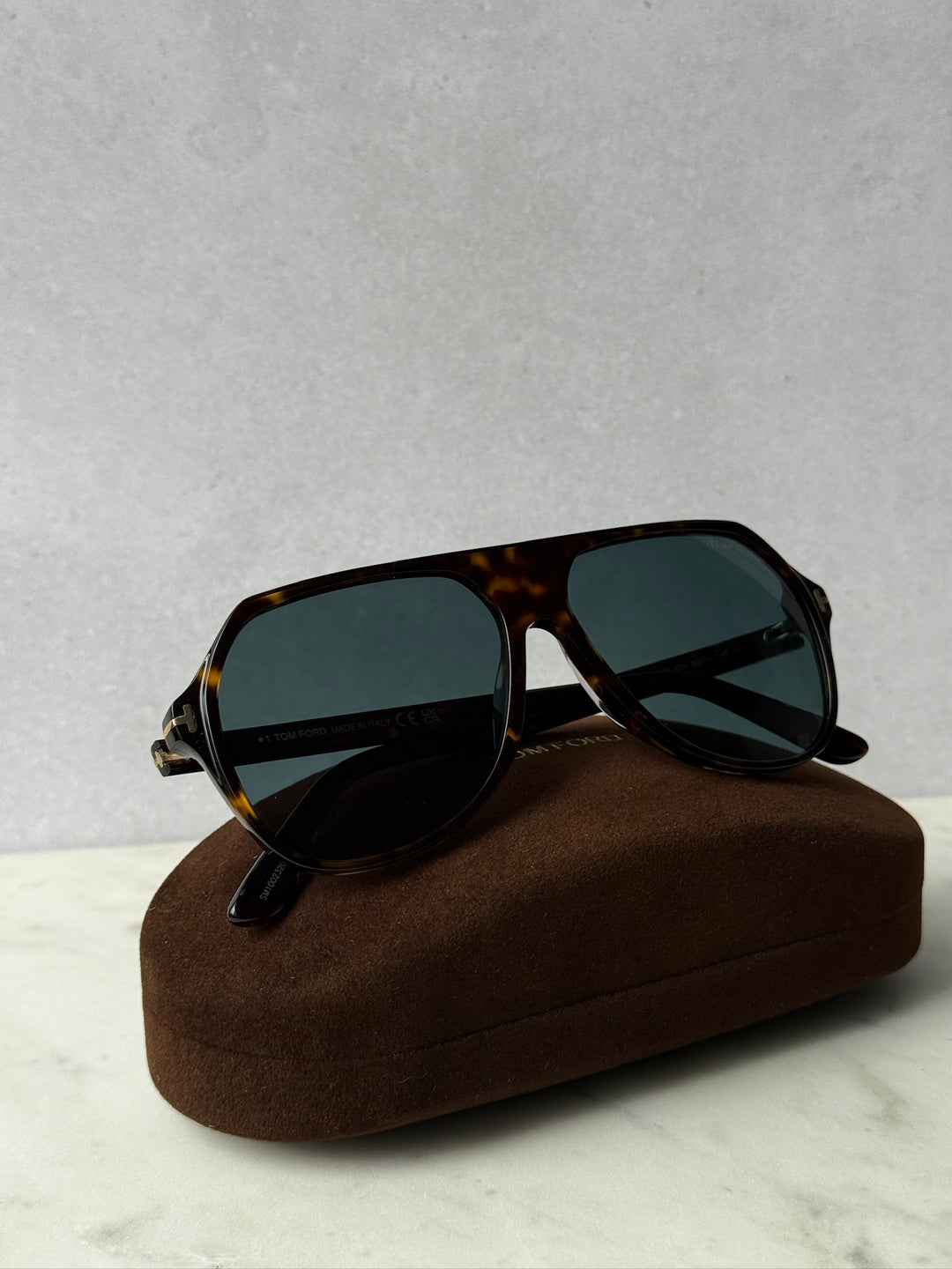Aviator sunglasses with dark Havana frame and green tinted lenses, beside brown case