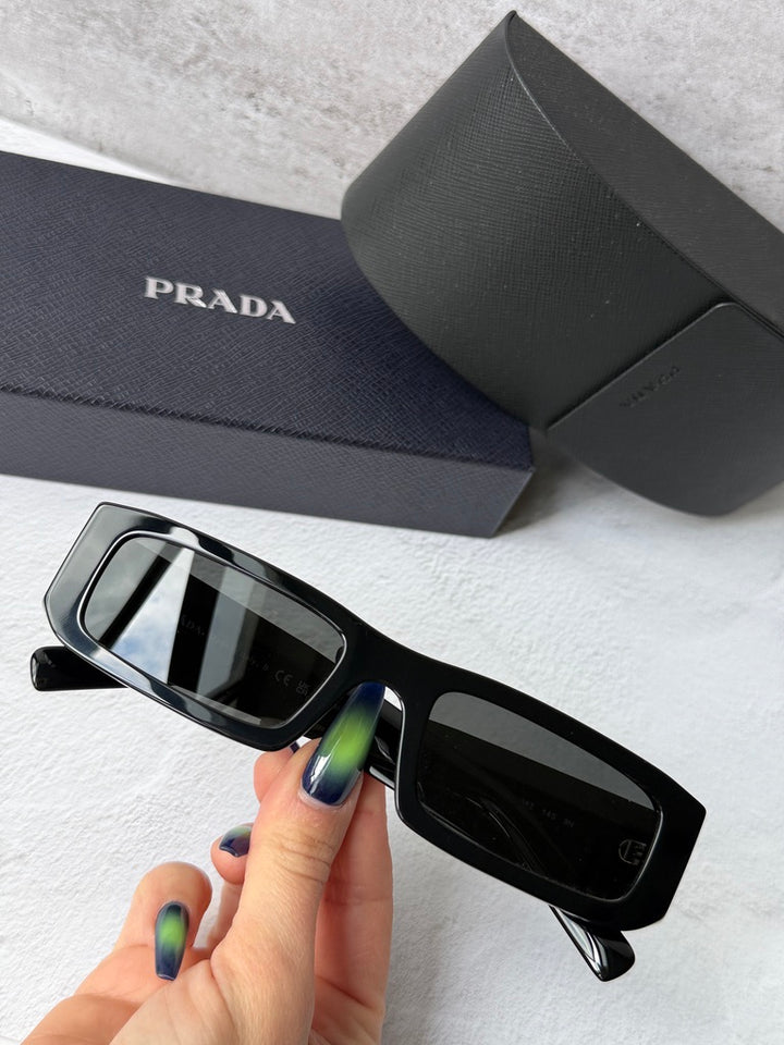 Prada black sunglasses with dark lenses, held near the frame and case.