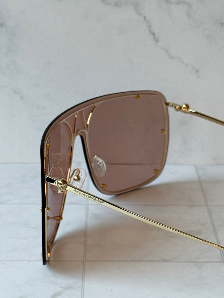 Close-up of nude oversized shield sunglasses with brown lenses and gold bridge