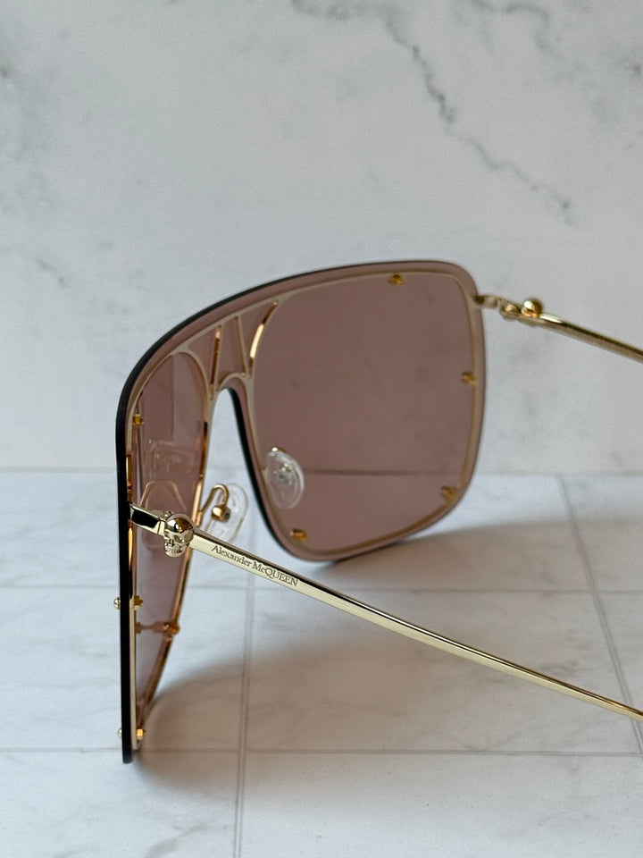 Close-up of nude oversized shield sunglasses with brown lenses and gold bridge