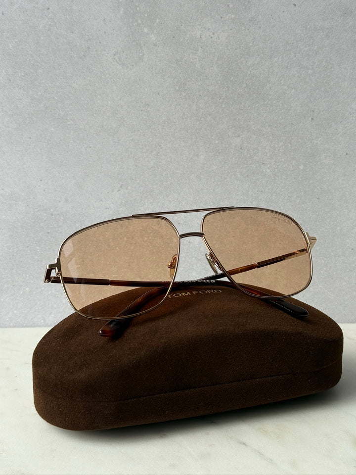 Gold photochromic sunglasses with tinted oval lenses and thin metal bridge, laid on case
