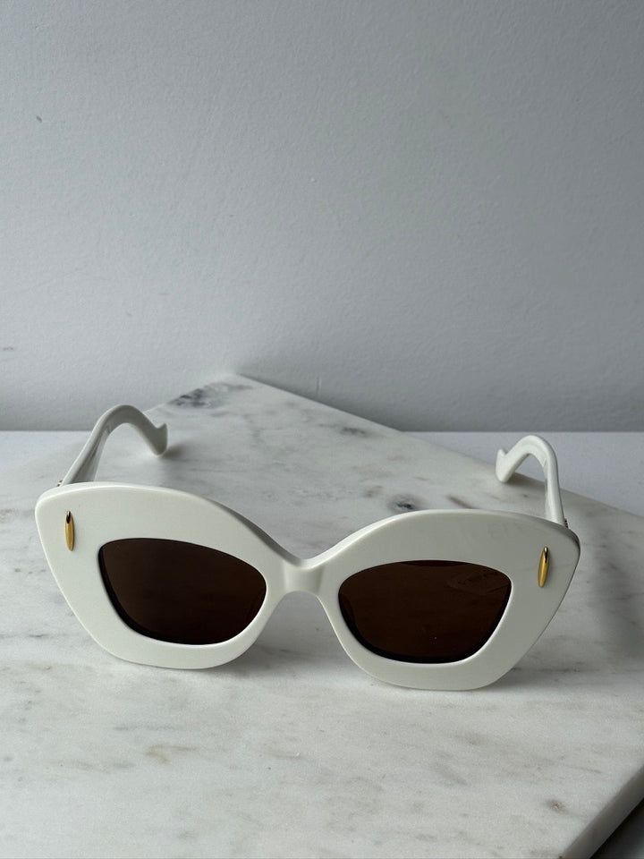 White cat-eye sunglasses with dark oval lenses and gold accents, front view