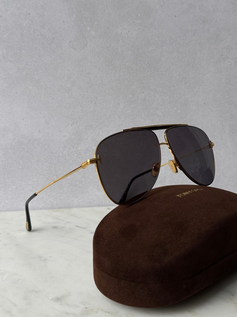 Gold aviator sunglasses with dark lenses, angled view over brown case