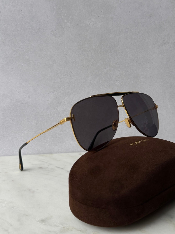 Gold aviator sunglasses with dark lenses, angled view over brown case