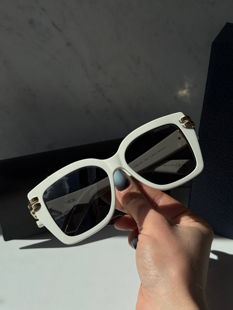Oversized butterfly sunglasses in hand, white frame with dark lenses and gold hardware