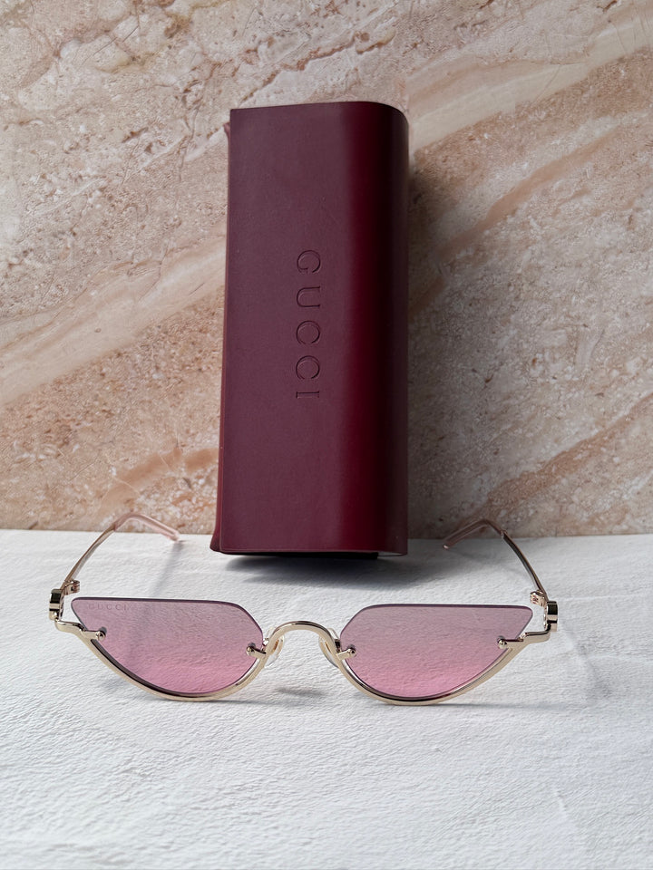 Gucci half-rim sunglasses with gold frame and pink tinted lenses near case