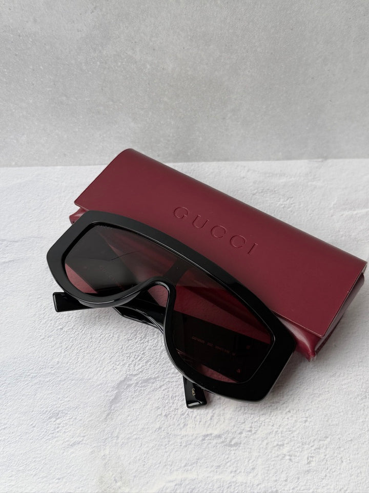 Oversized shield sunglasses, black frame with burgundy lenses, red carrying case