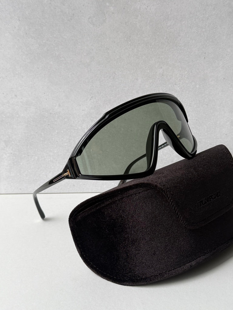 Black sunglasses with dark lenses and curved shield frame, beside black soft case